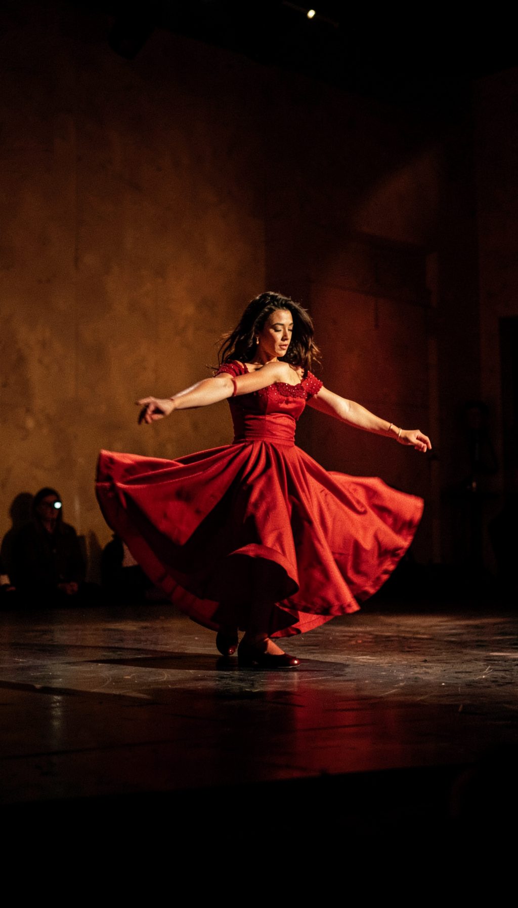 A dimly lit flamenco stage with a dancer in a flowing red dress mid-spin, dramatic shadows against warm ochre walls