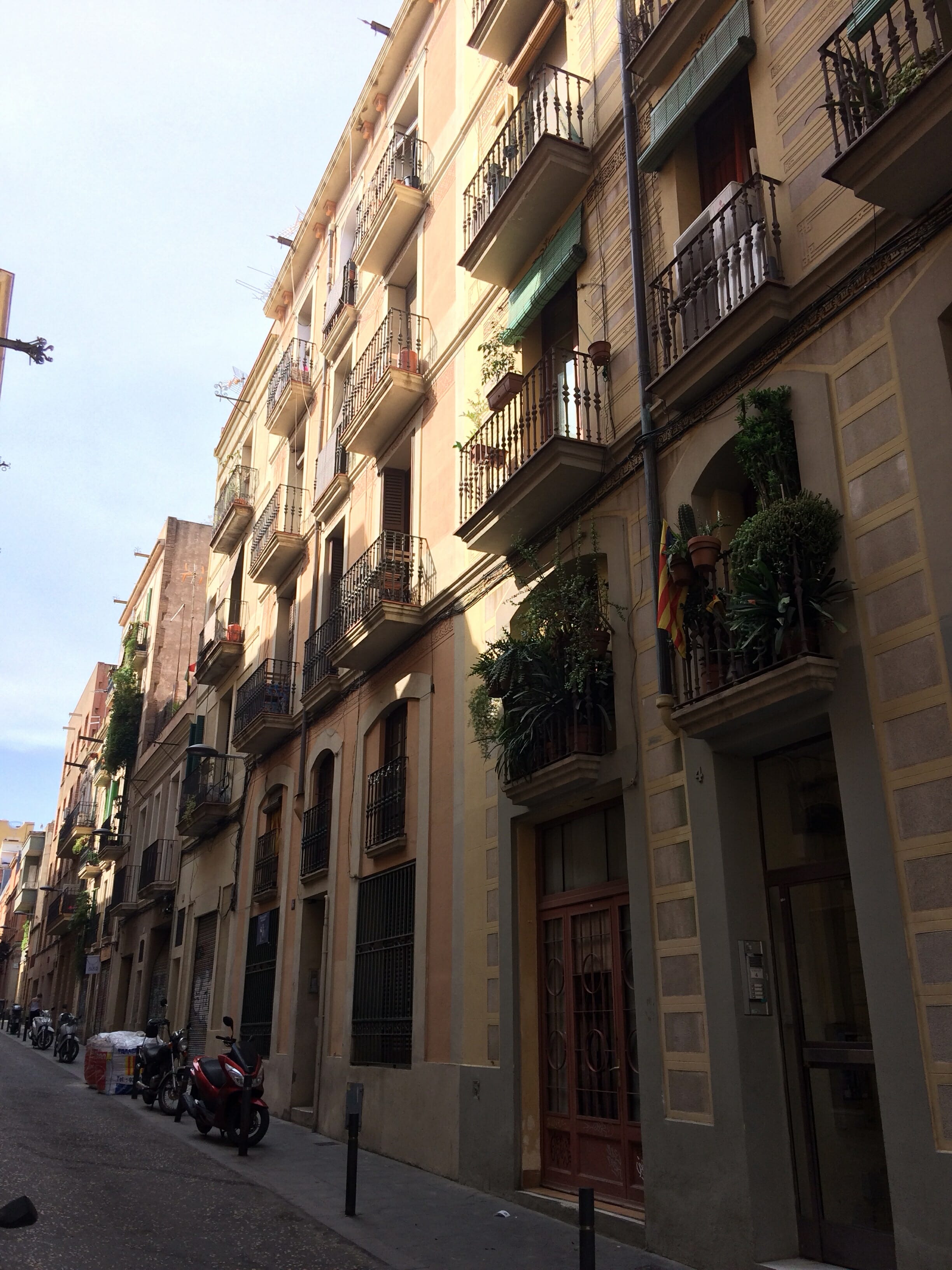Row of aged apartment buildings along a narrow street with balconies, plants, and parked motorbikes